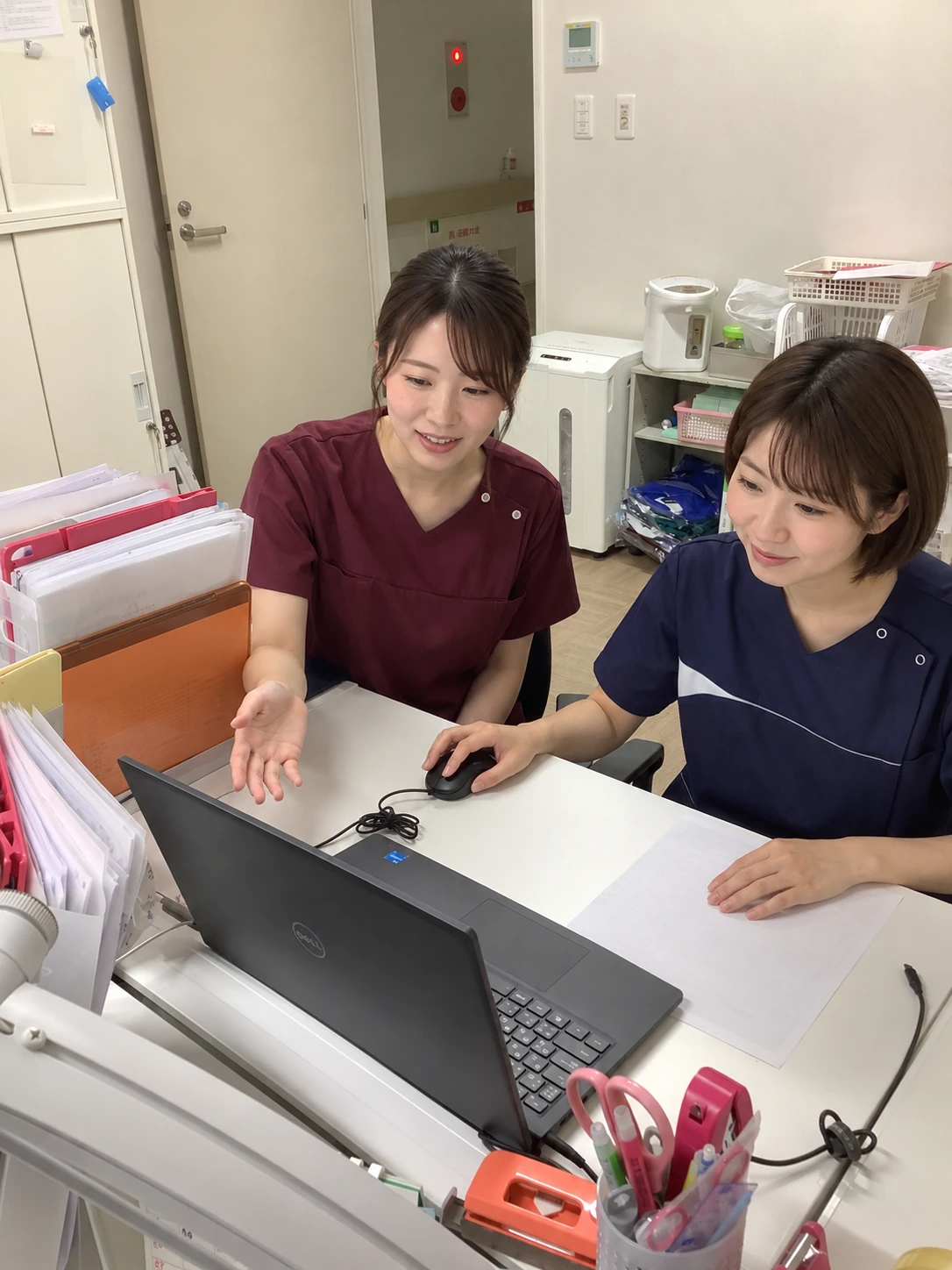 病院内の事務所で、画面を見ながら利用者さまのケアについて相談するスタッフのイメージ